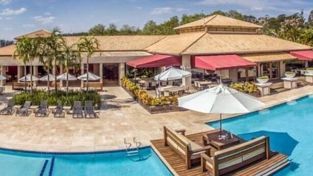 Un espace piscine avec des chaises longues et des parasols, une terrasse en bois et un bâtiment doté d’un toit en tuiles.