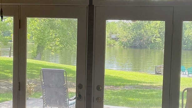 Une pièce dotée d’une porte-fenêtre coulissante qui donne sur une terrasse avec une chaise et une vue sur un lac.