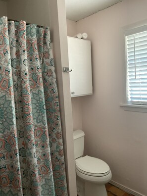 Ein Badezimmer mit Toilette, einem Schrank darüber und einem Fenster mit Jalousien.