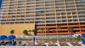 Un hotel de varios pisos con balcones, ubicación frente a la playa y zona de piscina con tumbonas.
