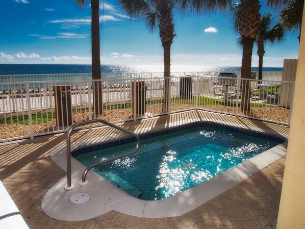 A swimming pool with a metal ladder, surrounded by a white fence, palm trees, and a view of the ocean. - Unit 704 3Br 3Ba Ocean Frt -Beach Service INCLUDED!! - Walk-in Shower! (Panama City Beach)