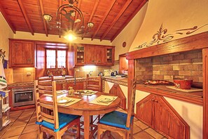 A kitchen with wooden cabinets, a dining table with blue chairs, and a brick fireplace. - Finca Los Viñedos (Tacoronte)