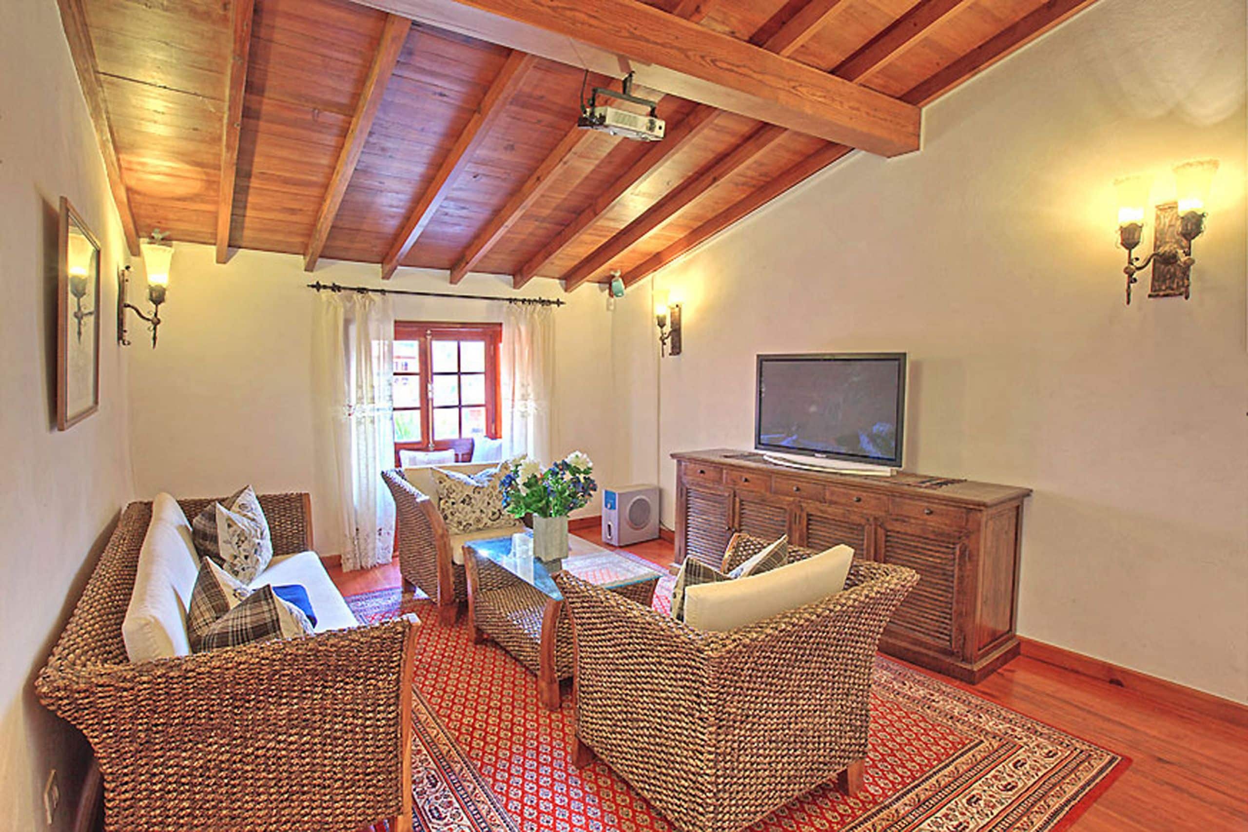 Una sala de estar acogedora con muebles de mimbre, un televisor y una alfombra roja con estampado.