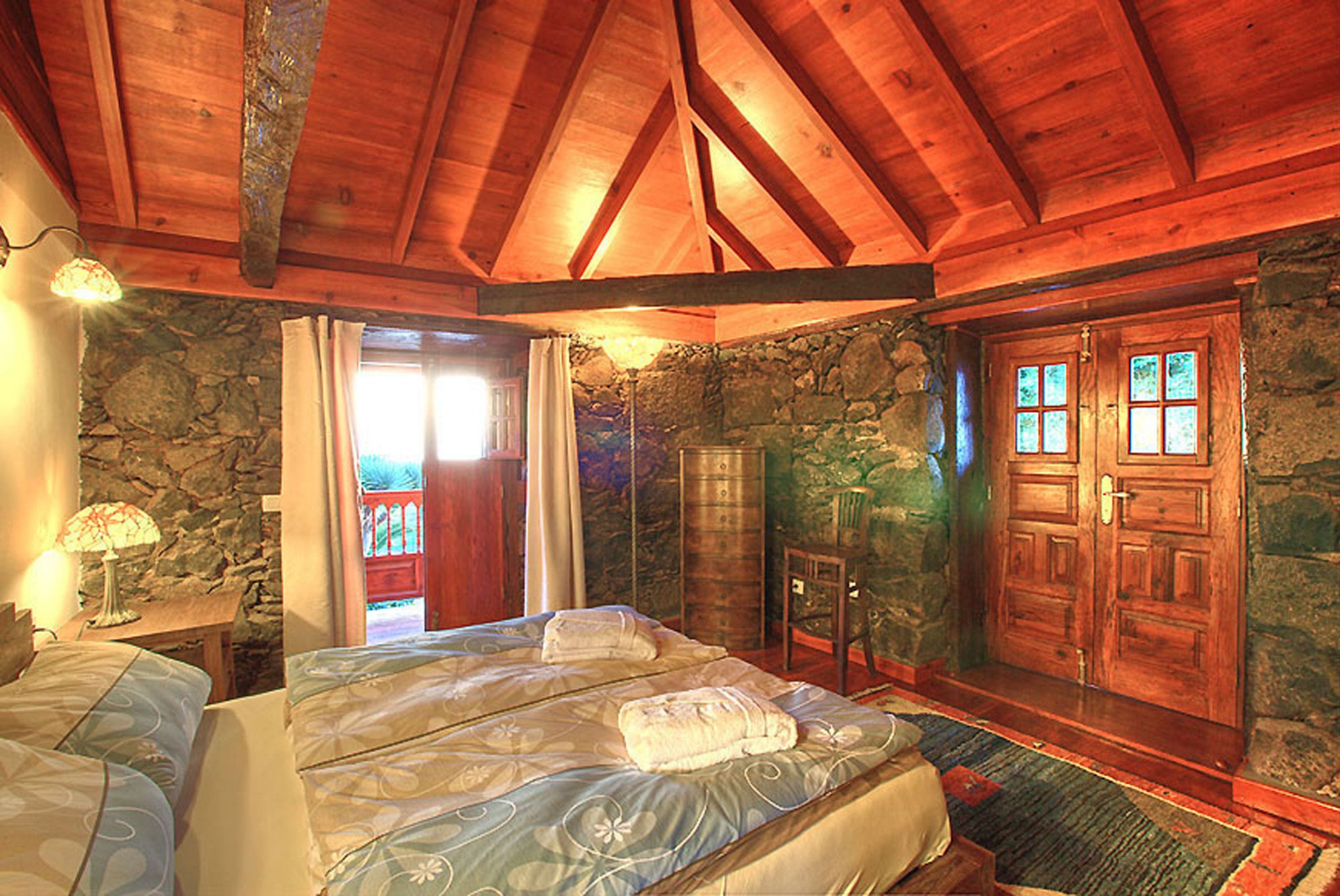 Un plafond en bois, un lit avec des oreillers, un mur en pierre et une porte en bois.