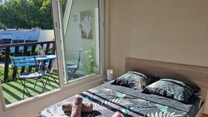 A bedroom with a bed, pillows, and a view of an outdoor area with a table and chairs. - Very nice T2 40m2 + 45m2 terrace (La Grande-Motte)