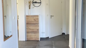 A modern hallway with dark tiled flooring, a wooden cabinet, a mirror, and a welcome sign. - Vacation apartment Winterscheid - Barrier-free in the countryside - near Cologne/Bonn (Ruppichteroth)