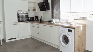 A modern kitchen with white cabinets, a built-in oven, a washing machine, and a wooden countertop. - Vacation apartment Winterscheid - Barrier-free in the countryside - near Cologne/Bonn (Ruppichteroth)