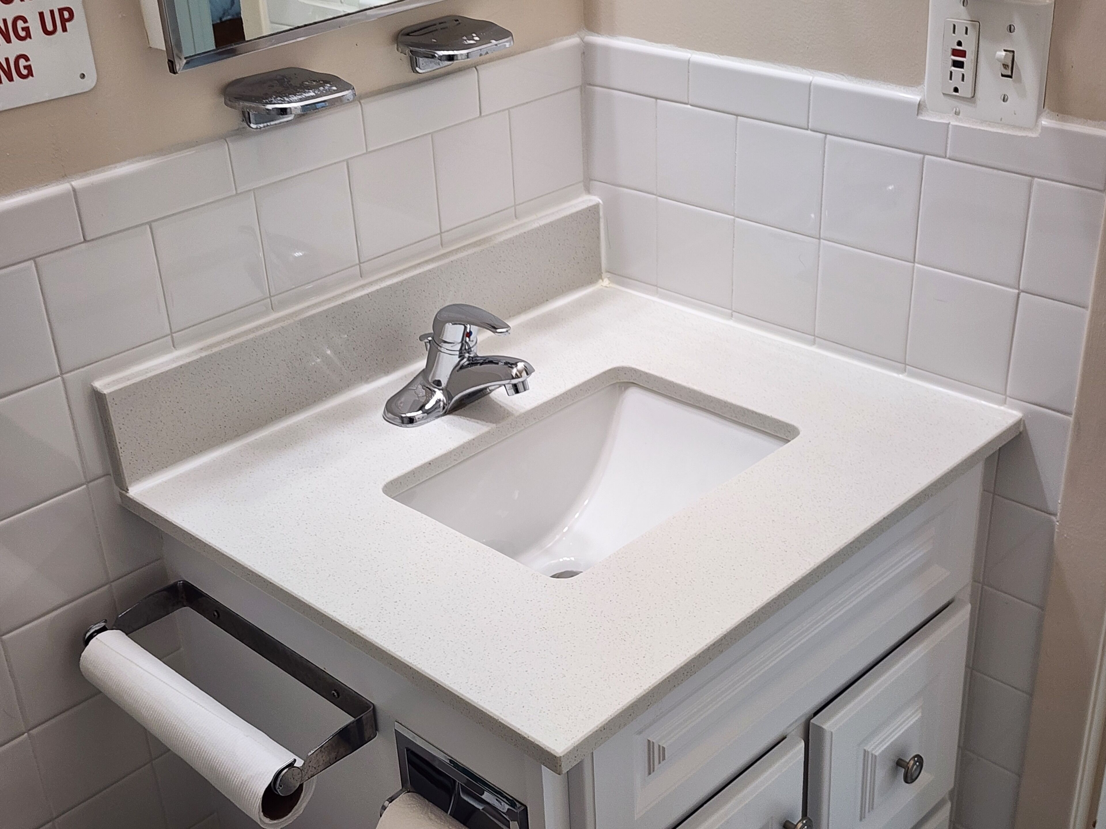 Une salle de bain avec un lavabo blanc, un miroir, un distributeur de serviettes et un porte-rouleau de papier toilette.