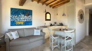 Eine moderne Küche mit Holzbalkendecke, ein Essbereich mit weißem Tisch und Stühlen sowie eine Couch mit Zierkissen.