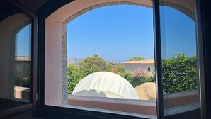 Blick aus einem Fenster auf eine weiße Kuppelstruktur im Freien, einen klaren blauen Himmel und Gebäude mit roten Ziegeldächern.