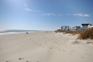En sandstrand med fotspår, en klar himmel och byggnader i bakgrunden.