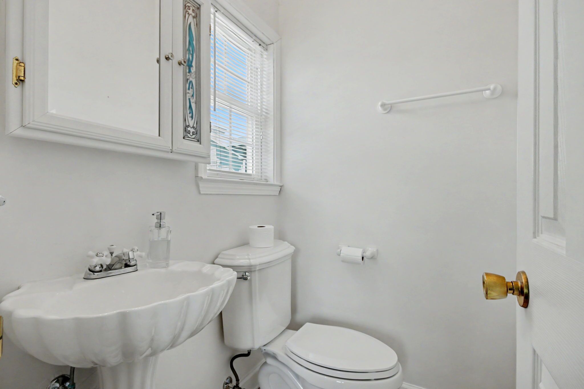 A bathroom with a white sink, toilet, and window with blinds.