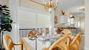 A dining area with a glass-top table, wicker chairs, a chandelier, and a view of the kitchen. - Cozy Beach House w/ Ocean Views & GREAT Amenities! (Myrtle Beach)