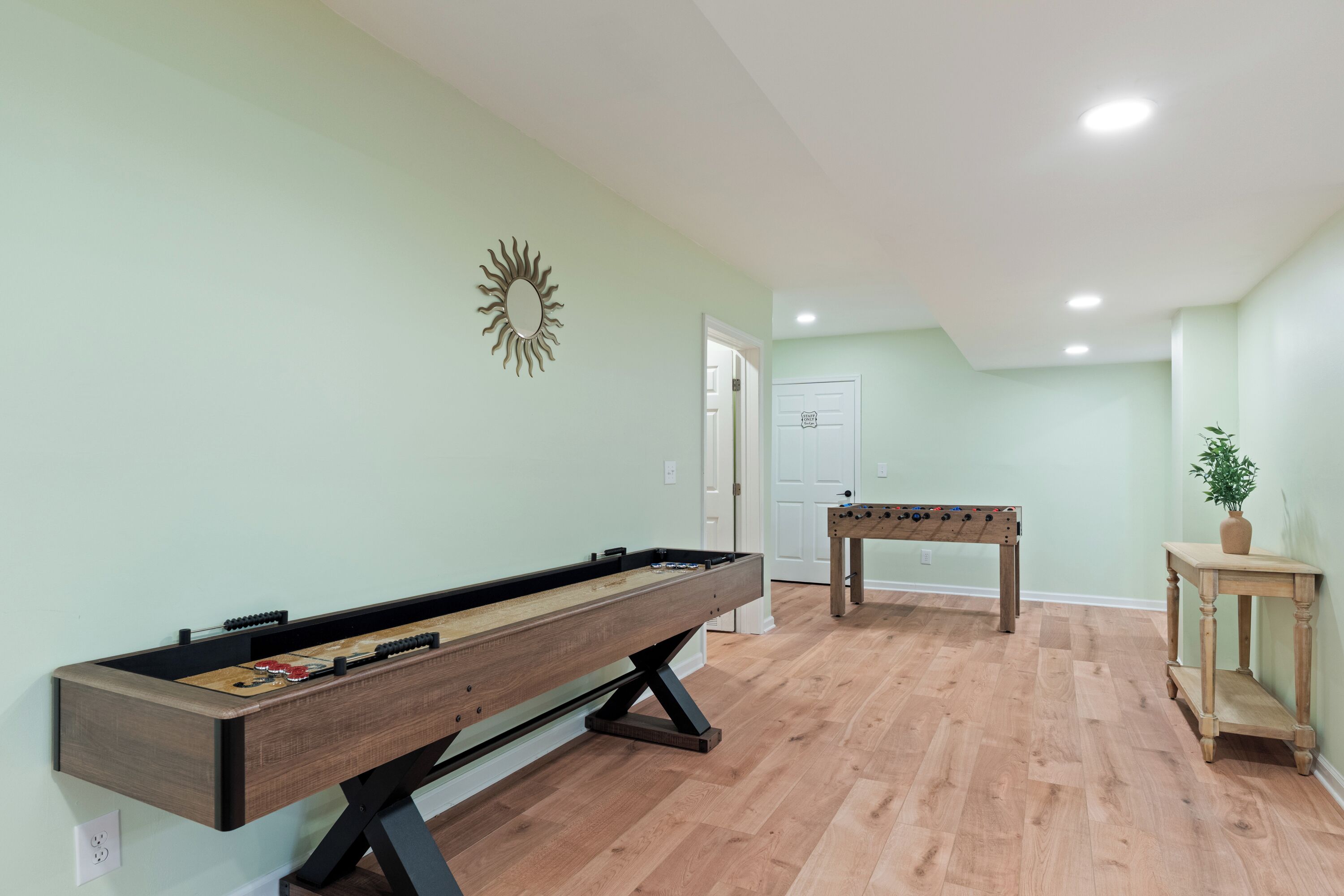 Una habitación con mesa de futbolín, mesa de billar y un adorno en la pared con forma de sol.