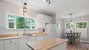 Eine moderne Küche mit weißen Schränken, einer Holzausziehtafel und einem Essbereich inklusive Tisch und Stühlen.
