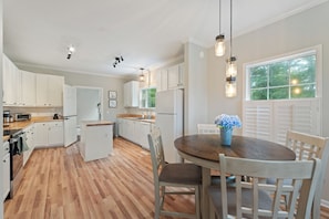 A kitchen with white cabinets, a wooden island, and a dining area with a round table and chairs.