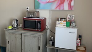 Una kitchenette con microondas, tostadora y refrigerador sobre una mesita, una cafetera y un vaso de agua en la encimera.