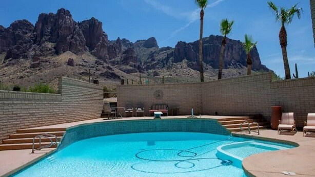 A swimming pool with a mountain backdrop, surrounded by palm trees and a brick wall. - Superstition Mountains Apache Junction - sleeps 16 (Apache Junction)