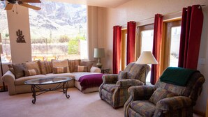 A living room with a sofa, armchairs, a glass coffee table, and a view of mountains through large windows. - Superstition Mountains Apache Junction - sleeps 16 (Apache Junction)
