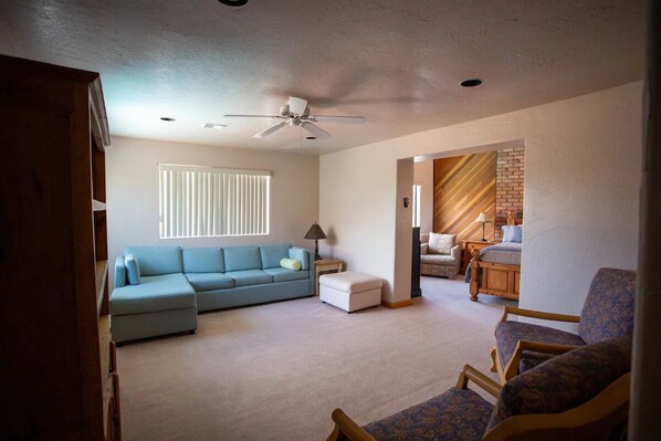 A spacious living room with a sectional sofa, a small table, and a ceiling fan.