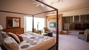 A four-poster bed with a patterned bedspread, a wooden dresser, a green armchair, and a brick wall with a television. - Superstition Mountains Apache Junction - sleeps 16 (Apache Junction)