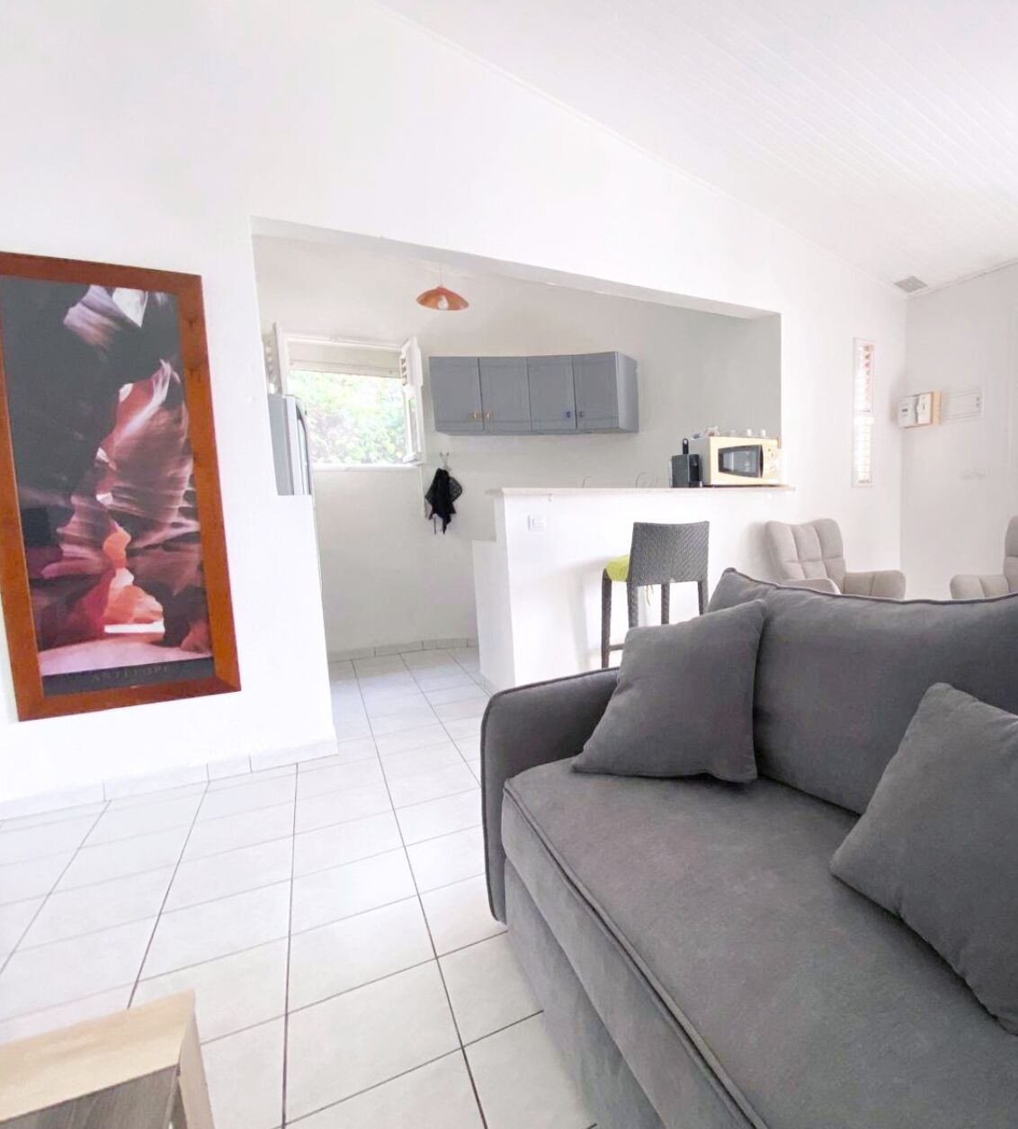 A modern living room with a grey sofa, a kitchen area with grey cabinets, and a small dining table.
