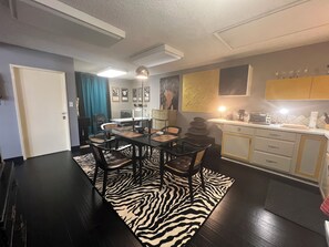 A modern kitchen with a dining area, featuring a zebra-patterned rug, dark wooden flooring, and a white door.