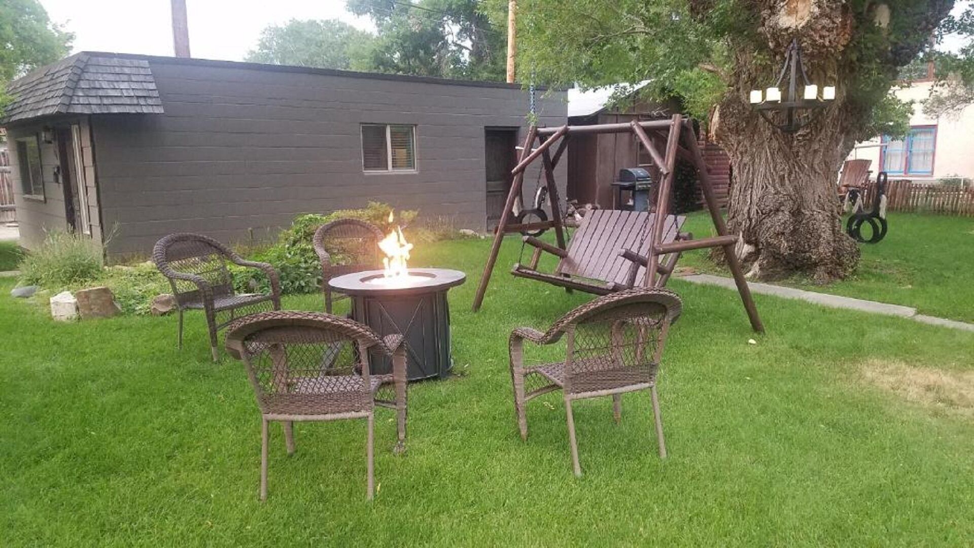 En trädgård med en eldstad, flätade stolar och en gunga.