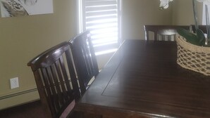 Comedor con una mesa de madera, sillas, una ventana con persianas, un colgante de luz y un cuadro en la pared.
