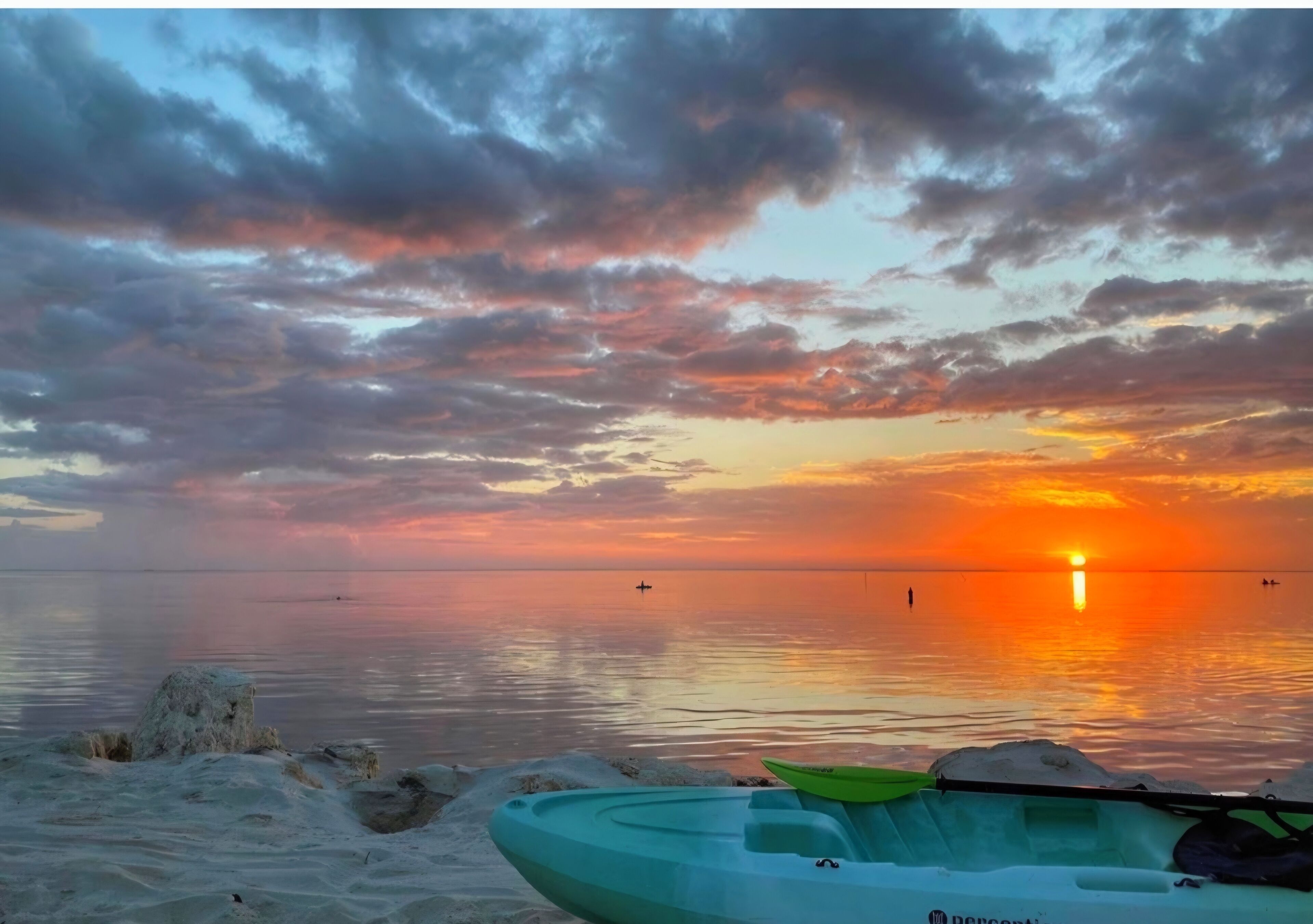 A sunset over a calm body of water with a kayak and a boat on the shore.