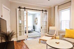 A living room with a sofa, a chair, a coffee table, and a TV. There is a sliding door leading to another room.