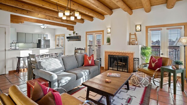 Un salón comedor amplio con chimenea, vigas de madera en el techo y una cocina al fondo.