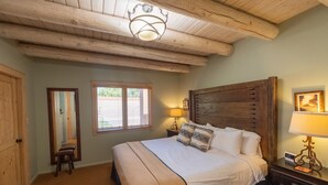 Une chambre à coucher avec un grand lit, une tête de lit en bois, une table de chevet avec une lampe, un miroir et une fenêtre.
