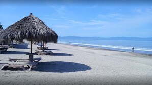 Una playa con sombrillas de paja y tumbonas.