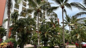 Un hotel de varios pisos, con palmeras y un estacionamiento.