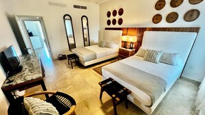 Habitación de hotel con cama, escritorio, silla, televisión y baño visible a través de una puerta abierta.
