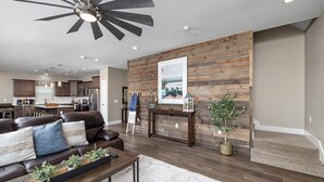 A modern living room with a brown leather sofa, a coffee table with plants, a wooden accent wall, and a ceiling fan. - Indoor/Outdoor Pool,Hot Tub, Firepit,Game Room, Pickleball, Pool Table,Lakeview (Branson)