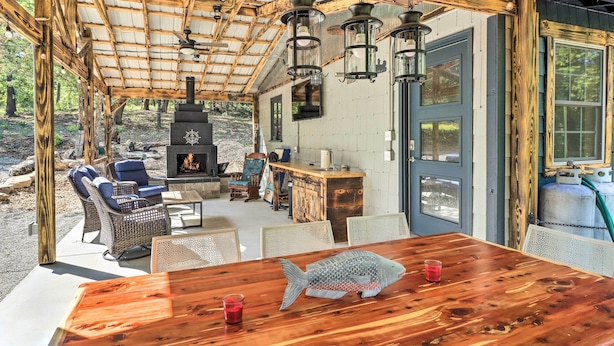 A rustic wooden cabin with a fireplace, outdoor seating, and a large fish decoration on the table. - Remodeled Cabin w/ Fire Pit on Norfork Lake! (Elizabeth)