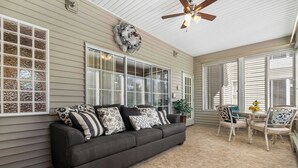 A covered patio with a dark gray sofa, white-framed windows, and a ceiling fan. - Legacy Walk-in - Golf Views Great Location (Branson)