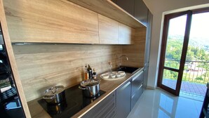A modern kitchen with a wooden backsplash, stainless steel appliances, and a large window offering a view of the outdoors. - Penthouse Andrea apartment with private pool (Meina)