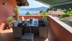 An outdoor dining area with a table set for four, surrounded by wicker furniture, overlooking a lake and hills. - Penthouse Andrea apartment with private pool (Meina)