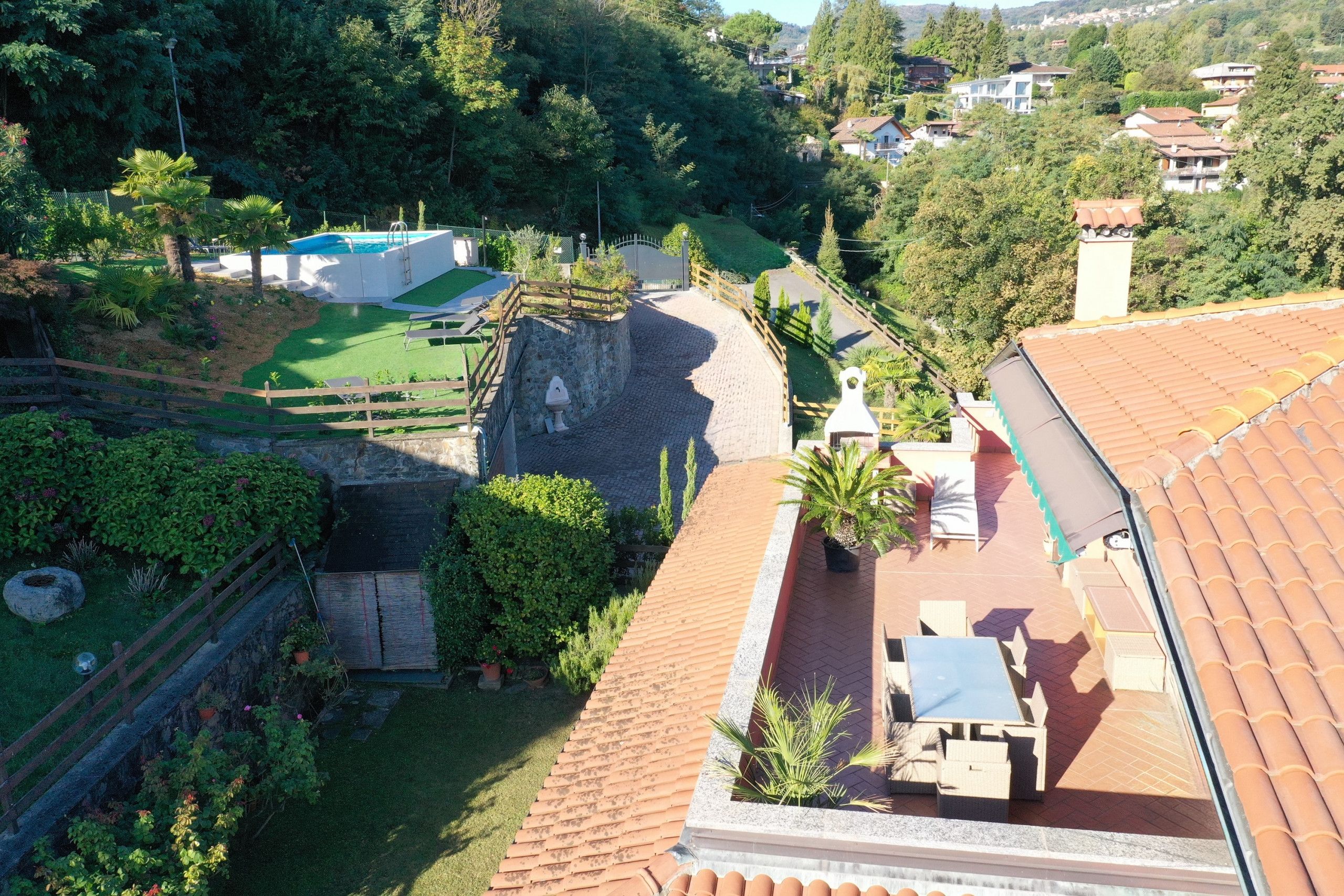 A rooftop terrace with a pool, surrounded by lush greenery and a stone wall.