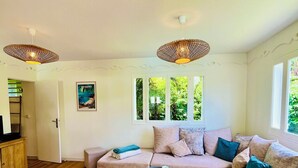 Ein geräumiges Wohnzimmer mit einer großen, beigefarbenen Eckcouch, zwei Beistelltischen und Holzboden. Zwei Pendelleuchten hängen von der Decke, und eine Tür führt in einen anderen Raum.