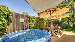 A backyard with a blue mosaic hot tub, a wooden fence, and a patio area with a table and chairs under a canopy.