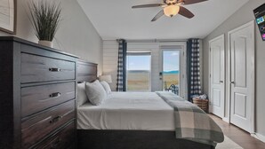 Une chambre à coucher comprenant un lit, une commode, un ventilateur de plafond et une vue sur l’extérieur par une porte.