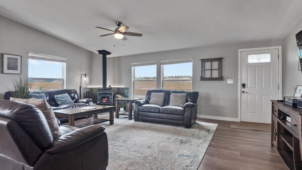 A spacious living room with a fireplace, leather sofas, a coffee table, and a large window offering a view of the outdoors.