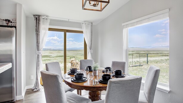 Un coin repas avec une table ronde dressée pour six personnes, de grandes fenêtres donnant sur l’extérieur et un lustre moderne.
