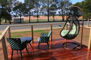 A wooden deck with a hanging chair and two chairs, overlooking a dirt road and trees. - The Pink Lake Tiny House - 'sakura' (Lochiel)