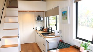 A compact kitchen with a microwave, sink, and wooden staircase. - The Pink Lake Tiny House - 'sakura' (Lochiel)
