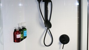 A shower with a rain showerhead, a handheld showerhead, and a control knob. There are three bottles of liquid soap on the wall. - The Pink Lake Tiny House - 'sakura' (Lochiel)
